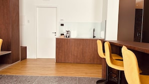 Eine moderne Küche mit einer Holzausziehtafel, einer Kaffeemaschine und einem Spülbecken. Im Essbereich befinden sich zwei gelbe Stühle und eine Holzbank.