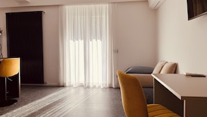 Ein modernes Hotelzimmer mit großem Fenster, Schreibtisch, Stuhl und einer Couch.