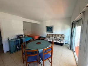 Un espacio habitable compacto con una mesa de comedor, sillas, sofá, cama, kitchenette y una puerta corrediza de vidrio.