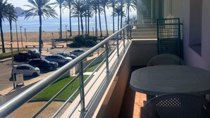 A balcony with a view of the beach, palm trees, and parked cars.
