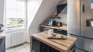 Eine moderne Küche mit Einbaukühlschrank, Mikrowelle und Kaffeemaschine. Ein Fenster bietet Blick auf die Stadt, und ein kleiner Tisch steht mit einer Eierregal voller Teetassen darauf.