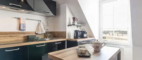 A modern kitchen with dark cabinets, a wooden countertop, and a dining table with a teapot and cup.