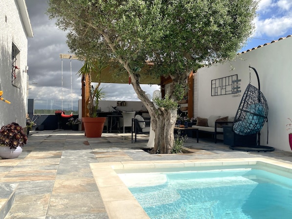 Un área de piscina con un árbol, mobiliario exterior y una silla colgante.