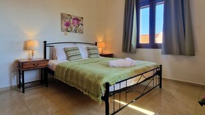 A bedroom with a bed, two bedside tables with lamps, a window with curtains, and a wall-mounted air conditioner. - Villa Sellia-Julie (Sellia)