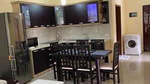 A modern kitchen with dark cabinets, a built-in oven, and a dining area with a table and chairs.