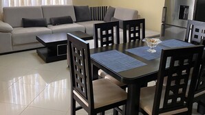 A modern living room with a sofa, dining table, chairs, and a refrigerator.