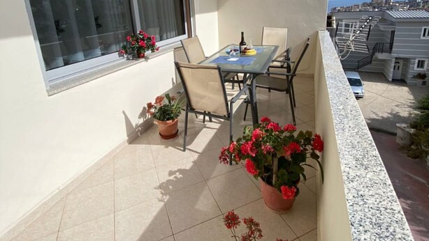 A balcony with a table and chairs, potted plants, and a view of the city.