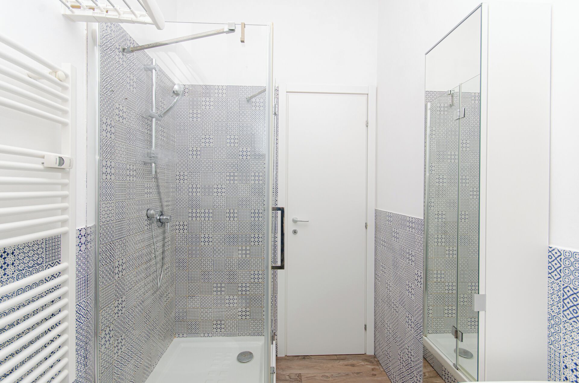 A bathroom with patterned tiles, a white door, and a glass shower enclosure.