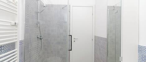 A bathroom with patterned tiles, a white door, and a glass shower enclosure.