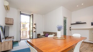 A modern living room with a wooden dining table, white chairs, a sofa, and a large window with a view of buildings. - VivimiHome-Stelvio House (Milan)