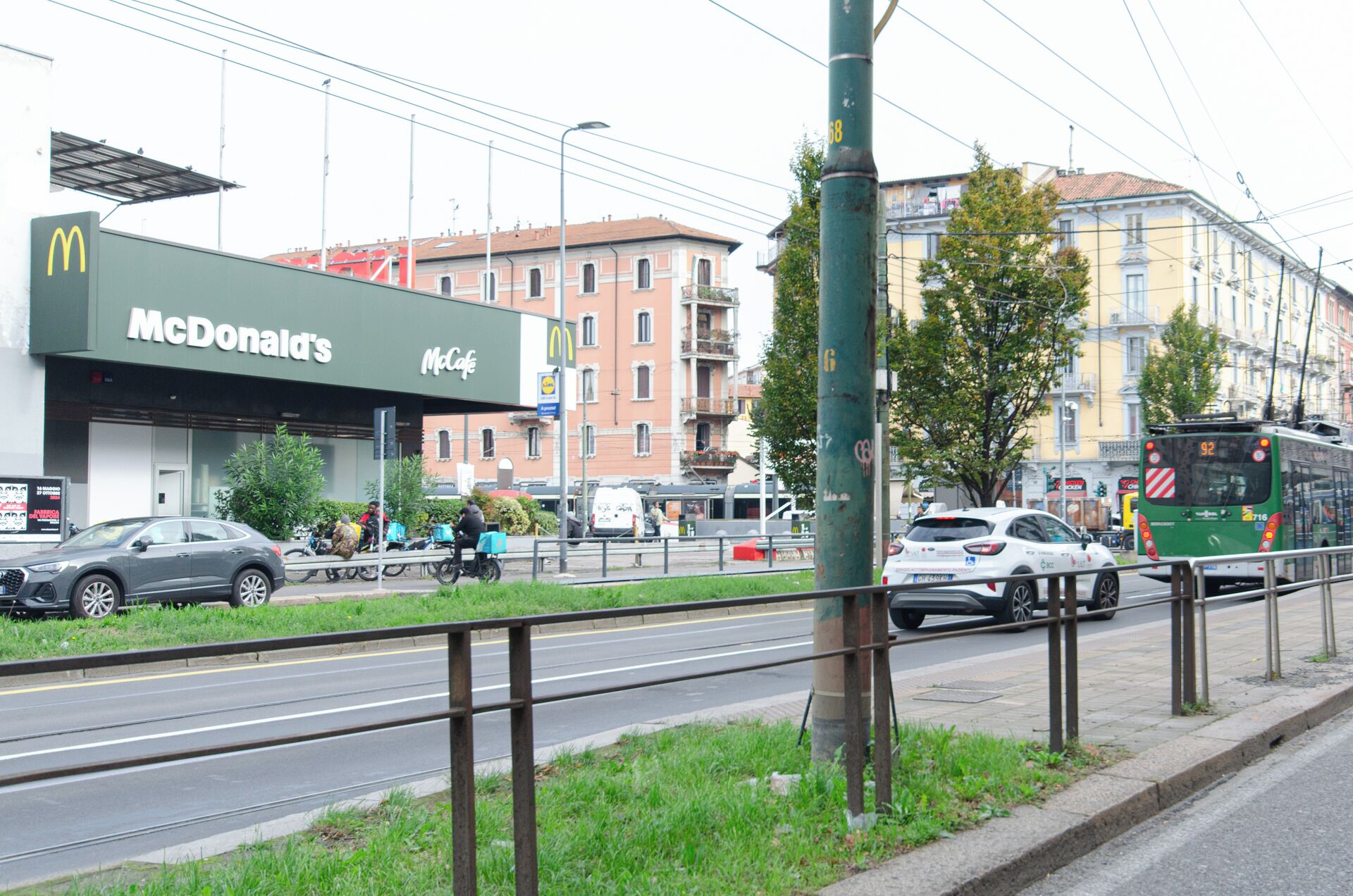 A McDonald's restaurant with a green facade, adjacent to a tram line and a road with vehicles.