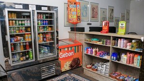 A small store with shelves stocked with various products, a refrigerator with beverages, and a Gebon sign. - Grande Hotel Paranavaí (Paranavaí)