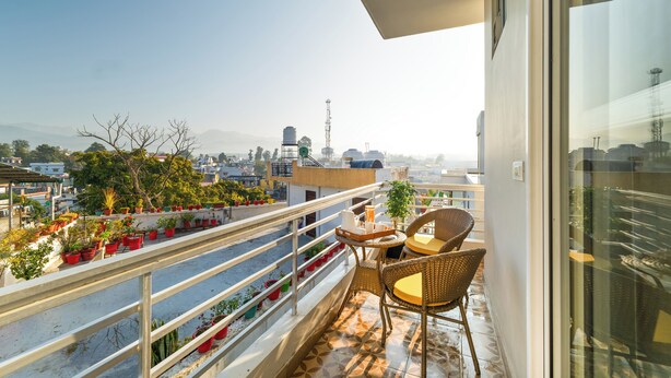 A balcony with potted plants, wicker chairs, and a view of the cityscape. - Auro Bliss - An Opulent 3bhk Penthouse in Dehradun (Dehradun)