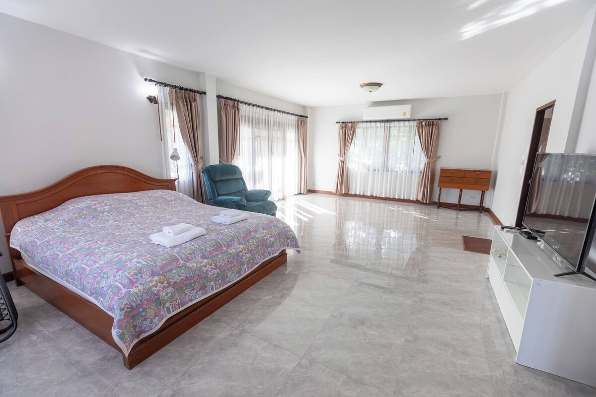 A hotel room with a large bed, a chair, a TV, and curtains.