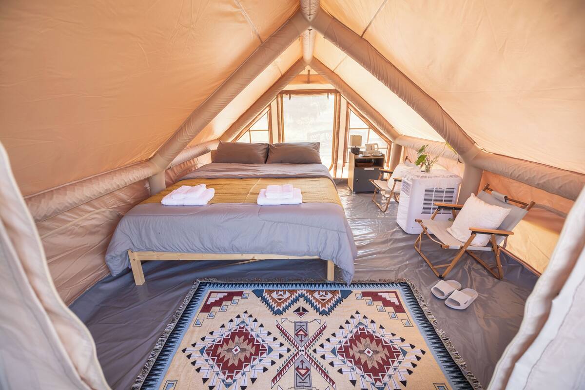 A cozy tented accommodation with a bed, a chair, and a small table.