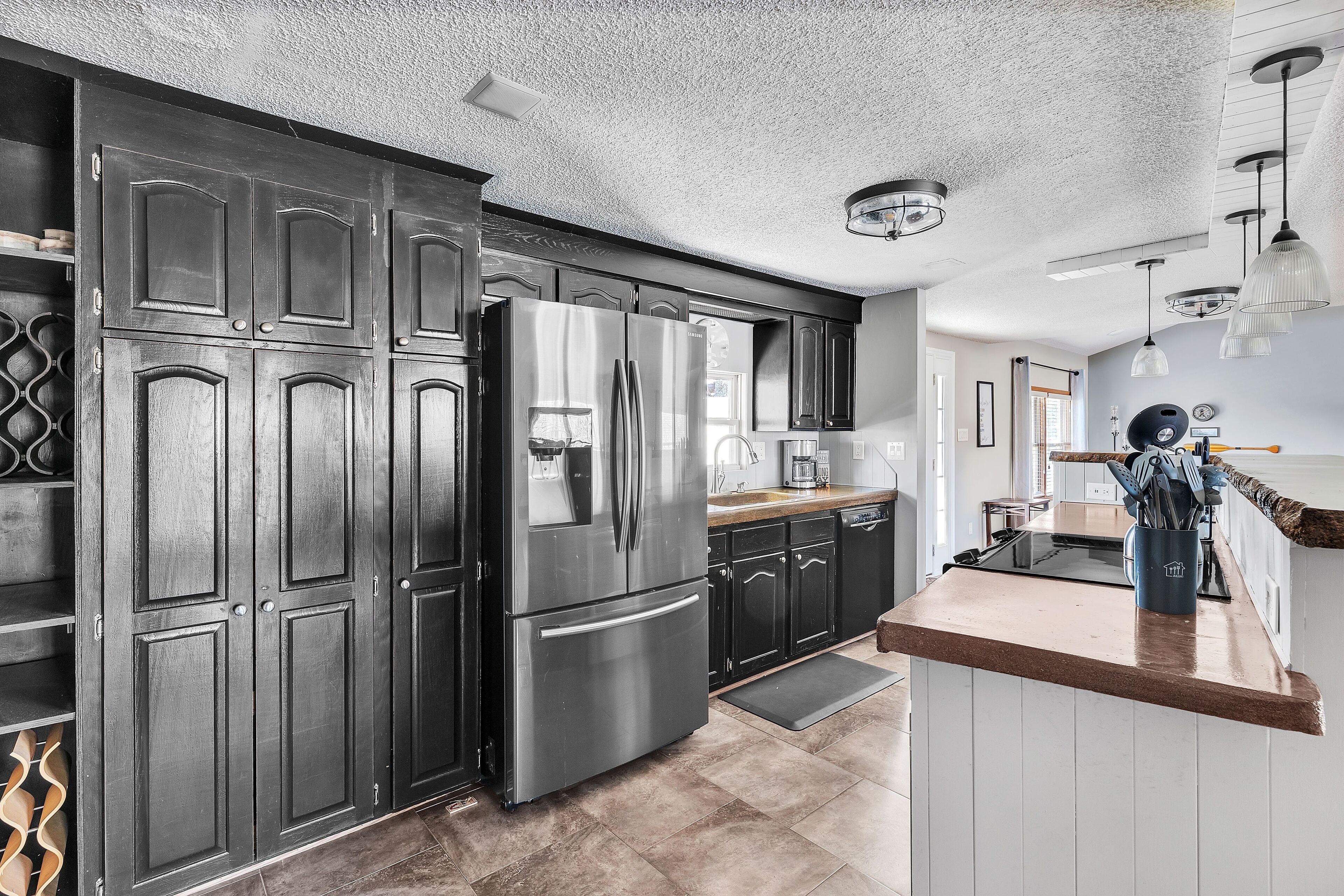A modern kitchen with dark cabinetry, stainless steel appliances, and a wooden countertop.