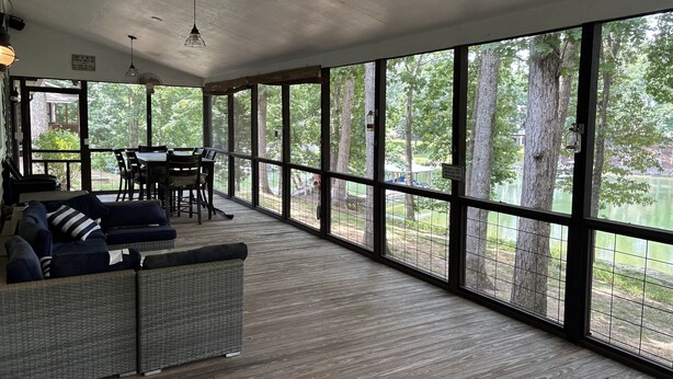Une pièce spacieuse dotée d’une grande fenêtre donnant sur un lac, d’une terrasse en bois et d’un coin salon avec un canapé et des fauteuils.