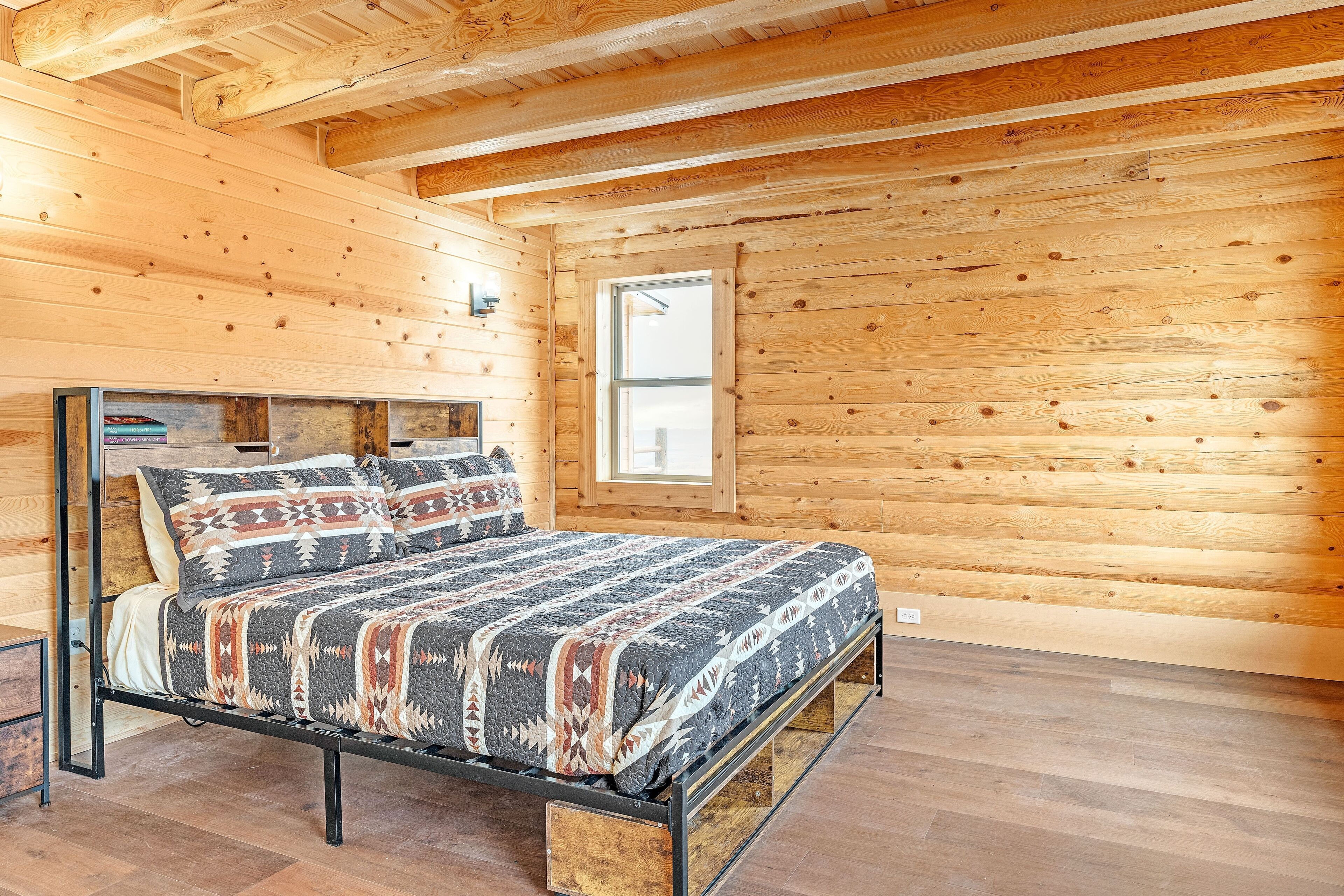 A wooden cabin bedroom with a bed, wooden walls, and a window.