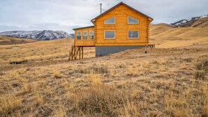 A wooden cabin with a simple design, situated in a dry, hilly landscape. - Mountain Cabin Near Trails, Skiing & Yellowstone 3 Bedroom Cabin (Belfry)
