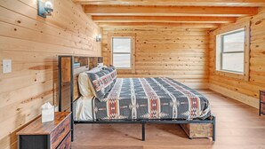 A wooden-paneled bedroom with a bed, a nightstand, and two windows. - Mountain Cabin Near Trails, Skiing & Yellowstone 3 Bedroom Cabin (Belfry)