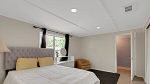 A bedroom with a bed, a bedside table, a mirror, a window with curtains, a chair, and a door leading to another room. - Ponderosa Off The Beaten Path 5 Bedroom Farmhouse 2.7 Acres by UF (Gainesville)