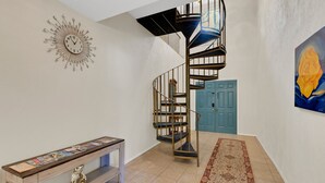 A spiral staircase with a blue door at the base, a wall clock, and a framed painting of a rose. - Ponderosa Off The Beaten Path 5 Bedroom Farmhouse 2.7 Acres by UF (Gainesville)