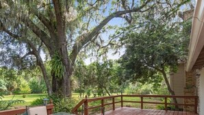 A wooden deck with a glass table and chairs, surrounded by trees and a brick wall. - Ponderosa Off The Beaten Path 5 Bedroom Farmhouse 2.7 Acres by UF (Gainesville)