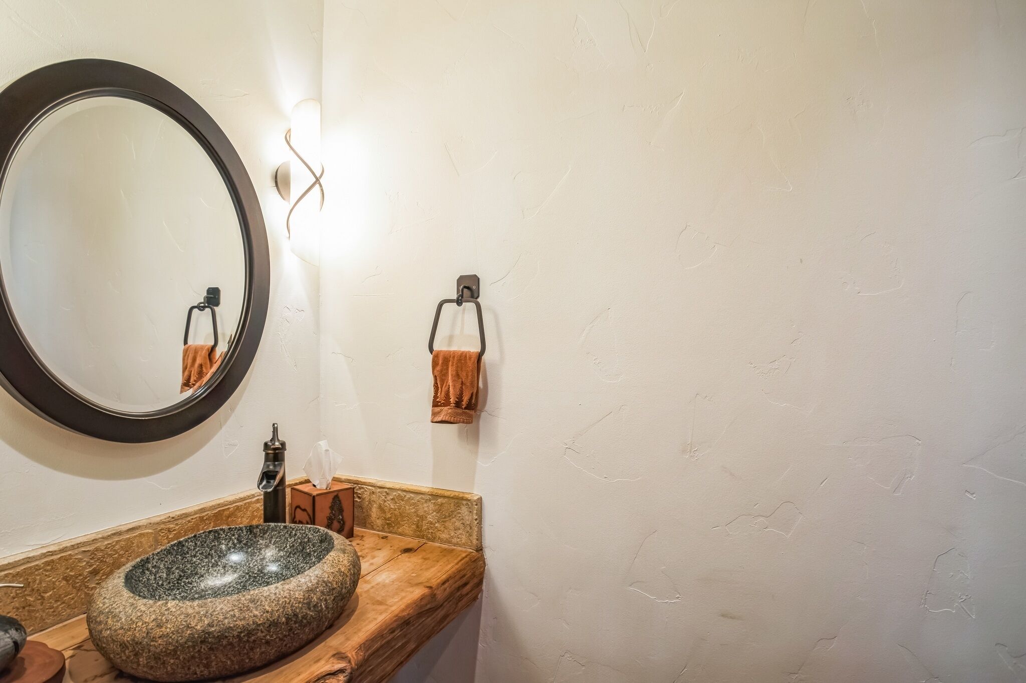 A bathroom with a round mirror, a stone sink, and a towel rack.
