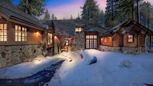 A log cabin with stone walls and a stone foundation, surrounded by snow and trees.