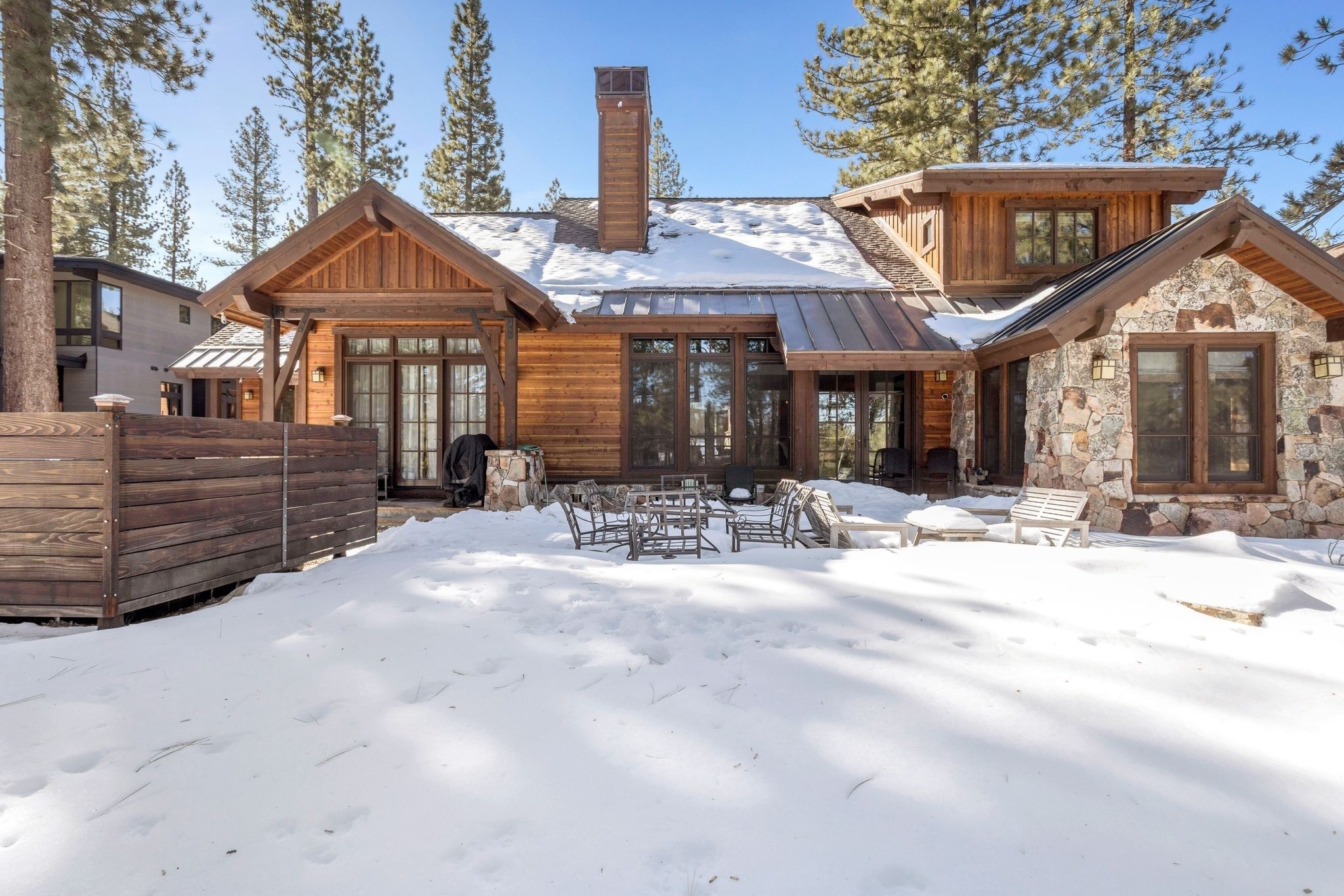 A wooden cabin with a stone exterior, large windows, and a covered outdoor seating area.