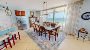 A modern kitchen with a dining area, a refrigerator, and a view of the ocean. - Oceania 504 3 Bedroom Condo (Destin)