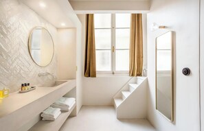 A modern bathroom with a large mirror, a sink with toiletries, a window with curtains, and a staircase. - JUST STEPS FROM ICONIC LOUVRE,JARDIN DES TUILERIES & PLACE VENDÔME–RUE DE RIVOLI (Paris)