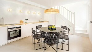 A modern kitchen with a round dining table, black woven chairs, and a hanging light fixture. - JUST STEPS FROM ICONIC LOUVRE,JARDIN DES TUILERIES & PLACE VENDÔME–RUE DE RIVOLI (Paris)