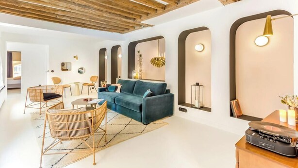 A modern living room with a blue sofa, wicker chairs, and a wooden ceiling. - JUST STEPS FROM ICONIC LOUVRE,JARDIN DES TUILERIES & PLACE VENDÔME–RUE DE RIVOLI (Paris)