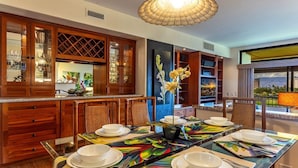 A dining area with a long table set for six, surrounded by wooden cabinets and a large window with a view.