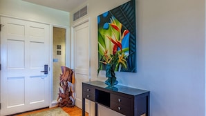 A hallway with a white door, a decorative wooden sculpture, a glass console table, and a colorful abstract painting on the wall.