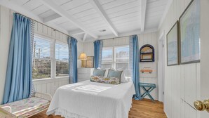 Un dormitorio con una cama, una mesita, una silla, una lámpara y una ventana con cortinas.