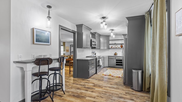 A modern kitchen with grey cabinets, a wooden floor, and a dining area with bar stools. - 3 Bedroom Family Home in Lake Charles, La (Lake Charles)