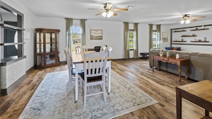 A spacious living room with a dining area, wooden flooring, ceiling fans, and a fireplace. - 3 Bedroom Family Home in Lake Charles, La (Lake Charles)