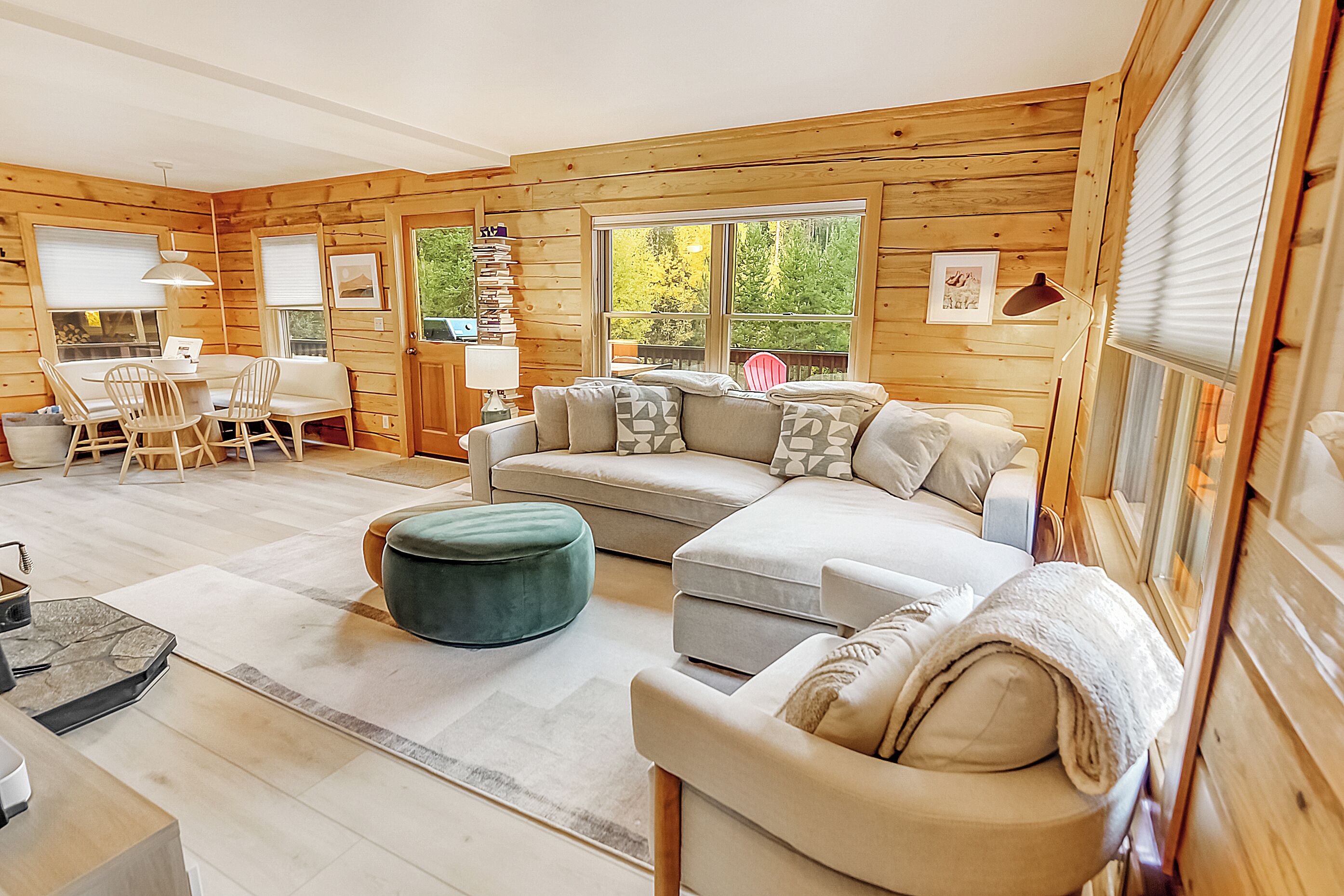 A cozy cabin interior with a sectional sofa, ottoman, and a dining area with chairs and a table.