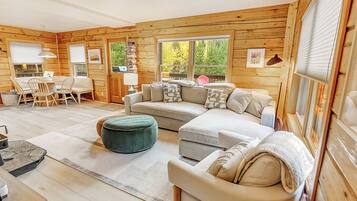 A cozy cabin interior with a sectional sofa, ottoman, and a dining area with chairs and a table.