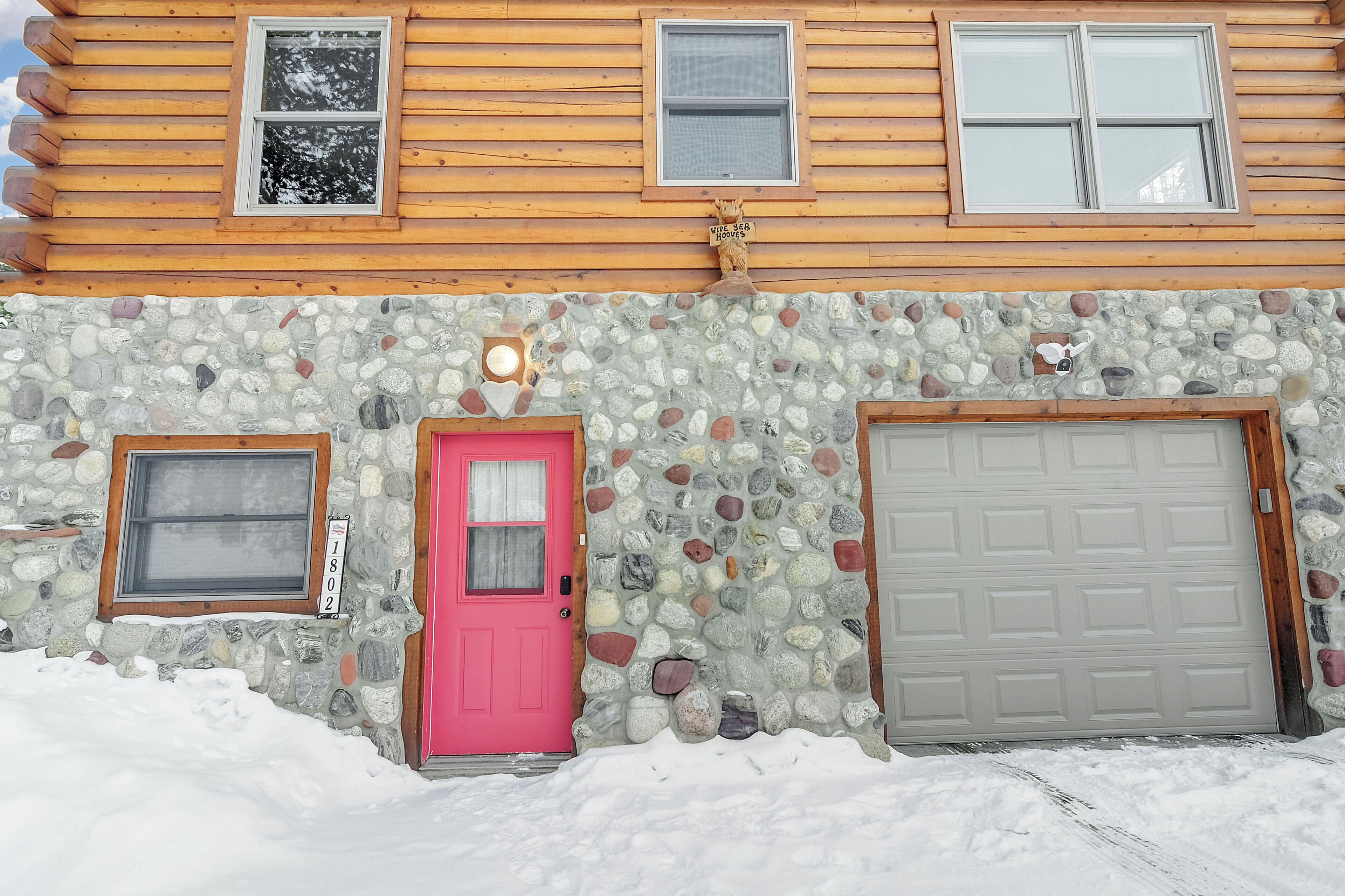 A log cabin with a stone facade, a pink door, and a garage door.