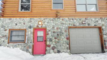A log cabin with a stone facade, a pink door, and a garage door.