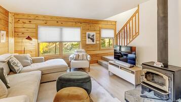 A cozy living room with a sofa, ottoman, TV, and a wood-burning stove.