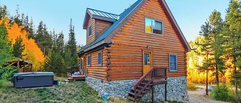 A log cabin with a stone foundation, a wooden deck, and a staircase leading to the entrance.