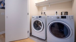 A laundry room with two front-loading washing machines and a shelf above them. - Modern Apt Downtown (Stamford, CT)