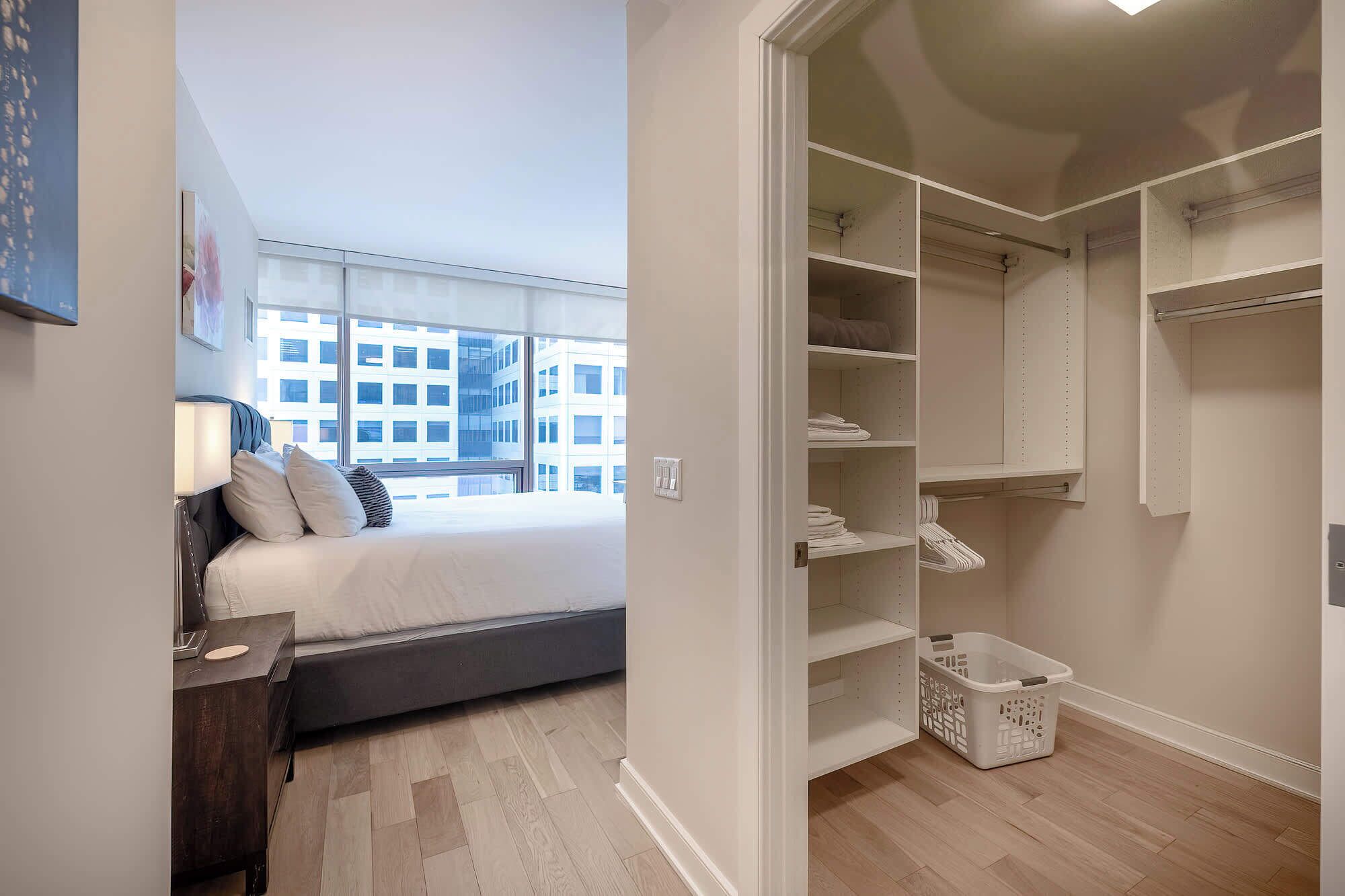 A bedroom with a bed, bedside table, and a view of a cityscape through large windows.