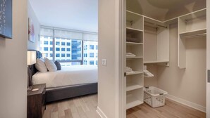 A bedroom with a bed, bedside table, and a view of a cityscape through large windows. - Modern Apt Downtown (Stamford, CT)