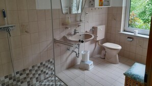 A bathroom with a shower, sink, toilet, and a window with a view of greenery. - Opas Hus auf Pellworm (Pellworm)