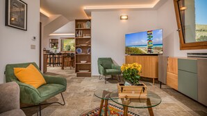 A modern living room with a green armchair, a glass coffee table, and a TV displaying a scenic view. - Villa sulla Roccia, privacy e relax. (Sicilia)